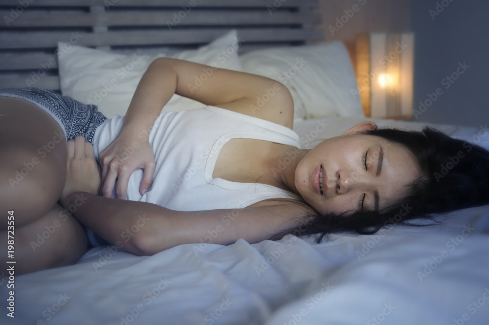 young beautiful and pretty Asian Chinese woman lying on bed feeling ill and unwell suffering belly and stomach cramp and menstruation period pain holding her tummy in female health concept young beautiful and pretty Asian Chinese woman lying on bed feeling ill and unwell suffering belly and stomach cramp and menstruation period pain holding her tummy in female health concept