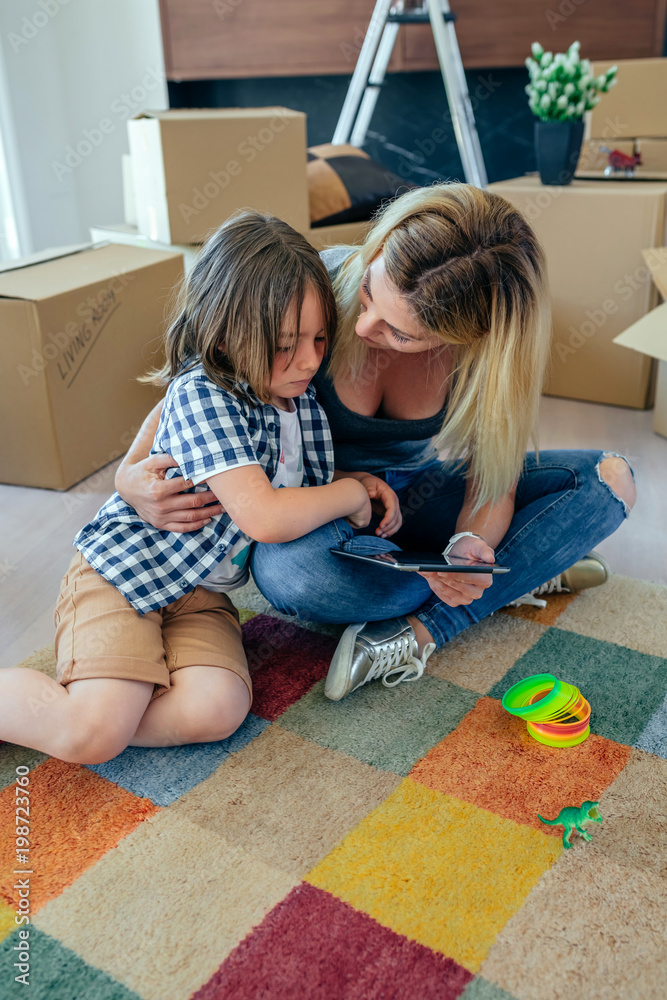Mother comforting her sad son sitting on the carpet while resting from doing the move Mother comforting her sad son sitting on the carpet while resting from doing the move