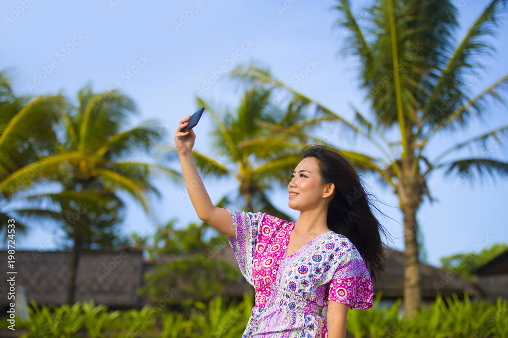 young happy beautiful and gorgeous Asian Chinese woman in glamour dress taking self portrait selfie photo with mobile phone camera at Summer tropical beach resort with palm trees young happy beautiful and gorgeous Asian Chinese woman in glamour dress taking self portrait selfie photo with mobile phone camera at Summer tropical beach resort with palm trees
