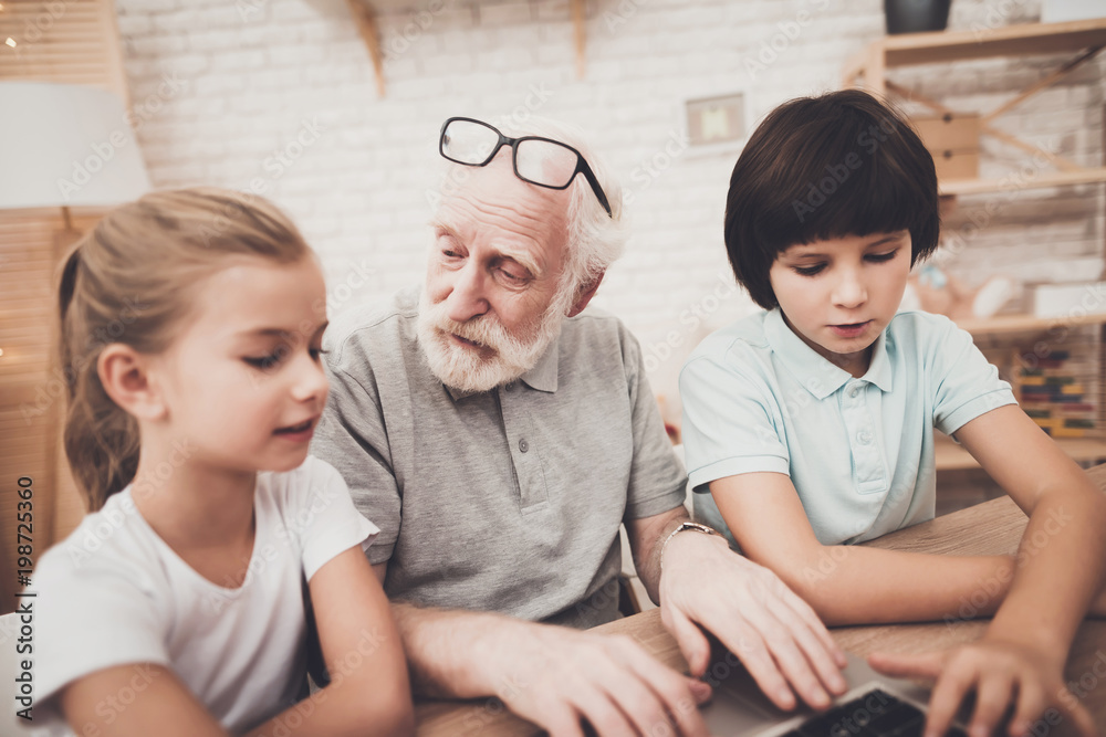 Grandfather, grandson and granddaughter at home. Grandpa and children are using laptop. Grandfather, grandson and granddaughter at home. Grandpa and children are using laptop.