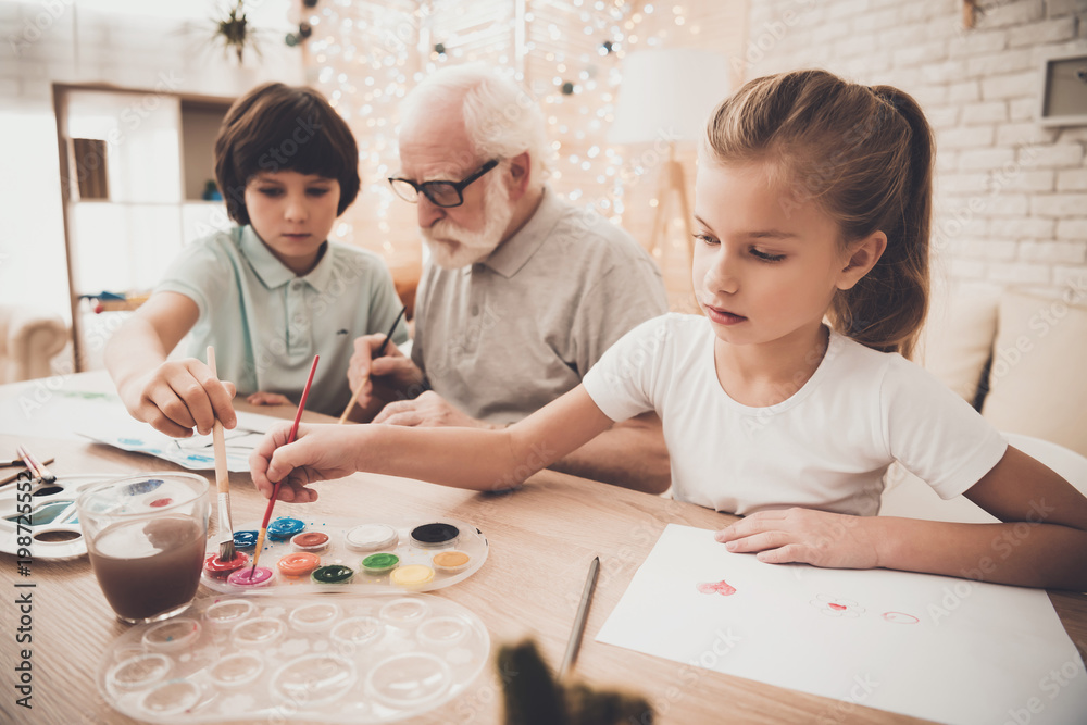 Fototapeta premium Grandfather, grandson and granddaughter at home. Children are painting with brushes.