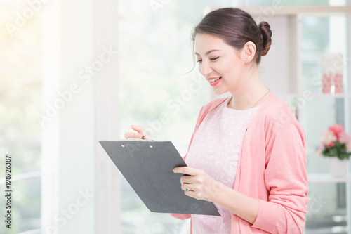 Business woman standing working near a window and holding clipboard at office.