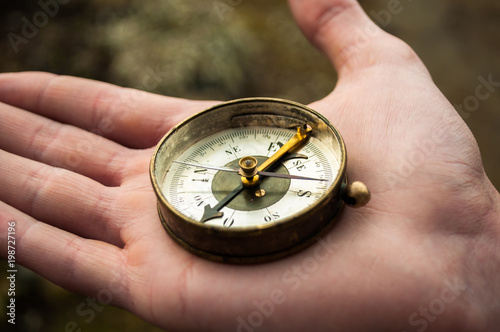 Closeup of hand holding old,magnetic golden compass and showing directions in the woods