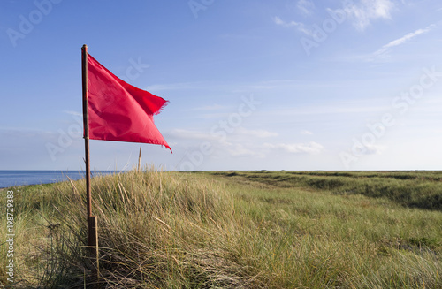Laesoe / Denmark: The frayed red flag in the dunes at Bloeden Hale is fluttering in the coastal wind