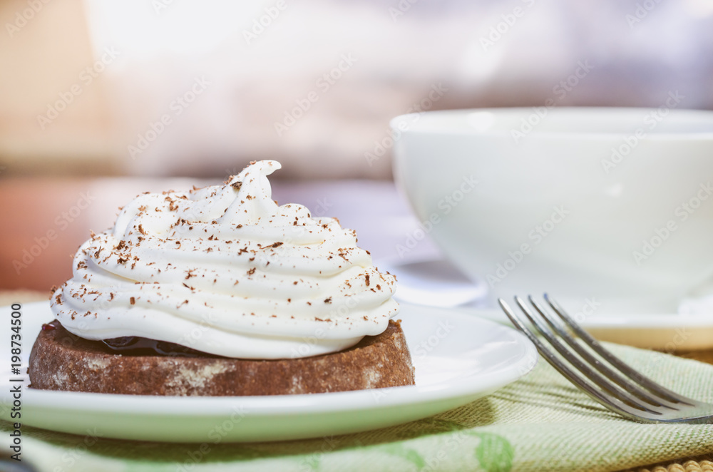 A chocolate cake with egg white cream, a cup of hot tea and a fork on a wooden table A chocolate cake with egg white cream, a cup of hot tea and a fork on a wooden table
