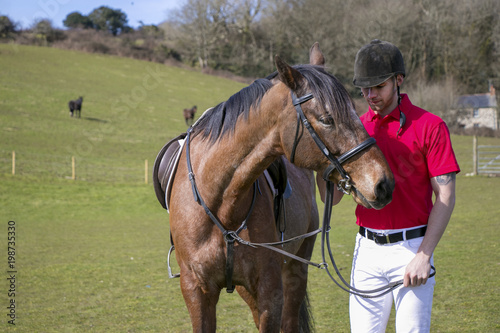 Rider on Horseback in field, wearing red polo shirt, white trousers,  black boots with horses in the background © Tony Marturano