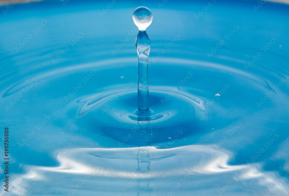 A falling drop in the blue water. The waves diverge from the drop