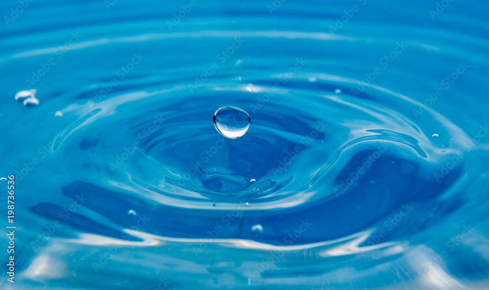 A falling drop in the blue water. The waves diverge from the drop A falling drop in the blue water. The waves diverge from the drop