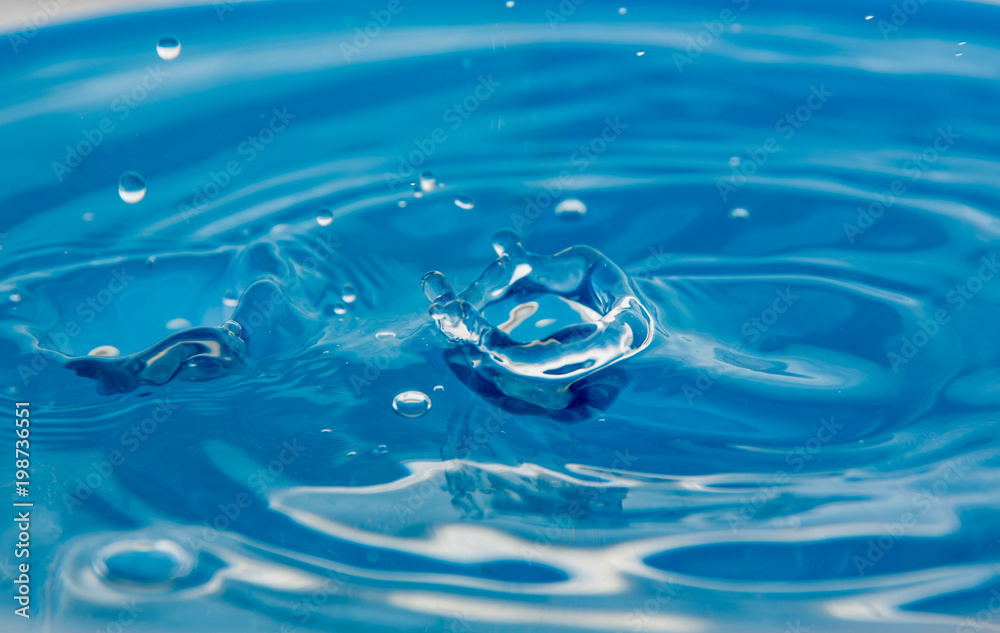 A falling drop in the blue water. The waves diverge from the drop A falling drop in the blue water. The waves diverge from the drop