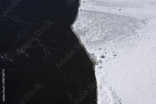 The landscape with the beach covered with snow and dark water