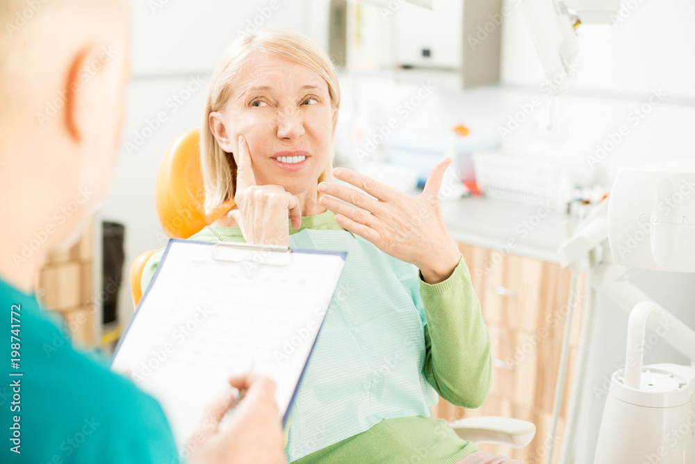 Mature patient complaining about pain in one of upper teeth during appointment with dentist Mature patient complaining about pain in one of upper teeth during appointment with dentist