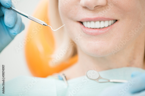Dental hook and mirror held by dentist and toothy smile of healthy patient