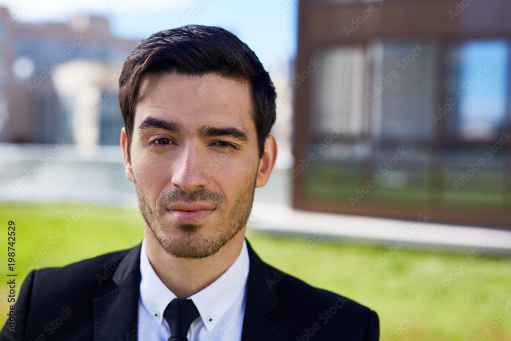 Young handsome businessman in elegant suit and tie looking at camera outdoors