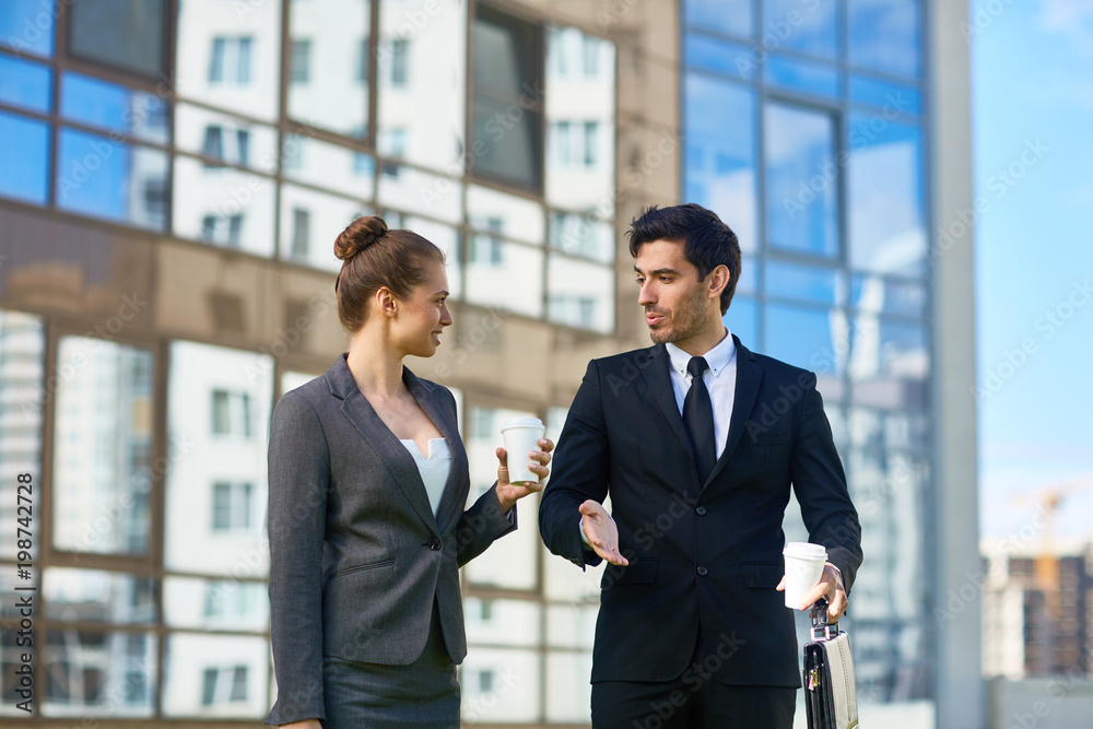 Two young elegant managers with drinks talking while walking home after work on summer day Two young elegant managers with drinks talking while walking home after work on summer day