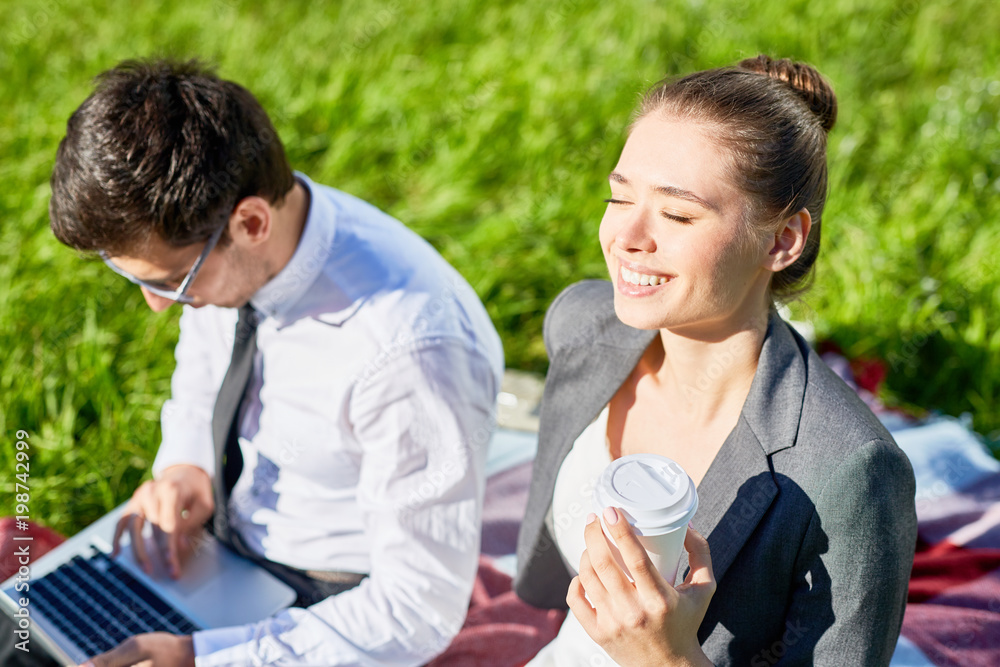 Young businesswoman with drink enjoying sunshine while her colleague networking near by Young businesswoman with drink enjoying sunshine while her colleague networking near by