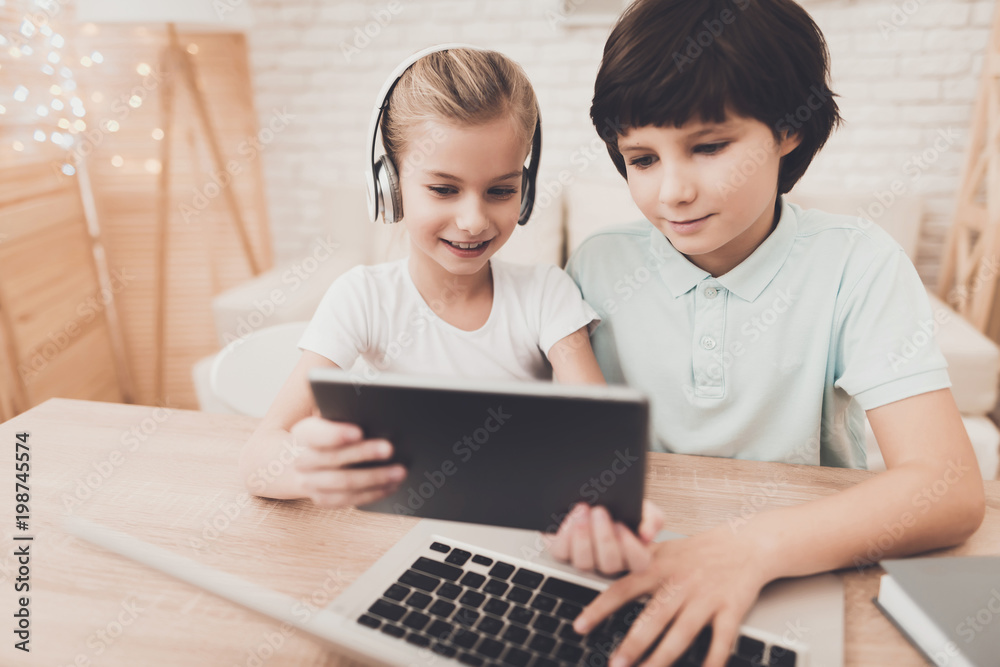Children at home. Brother and sister are using tablet and laptop in headphones. Children at home. Brother and sister are using tablet and laptop in headphones.