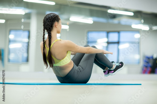 Young female doing exercise for belly muscles on the floor during workout