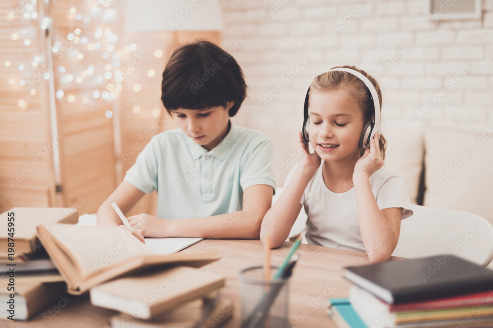 Children at home. Brother is writing and sister is listening to music. Children at home. Brother is writing and sister is listening to music.