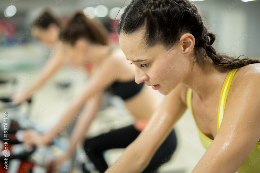 Tired and sweaty female training hard during workout on bike to get best results