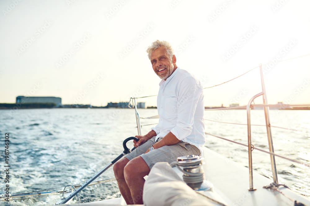 Smiling mature man sailing his boat along the coast Smiling mature man sailing his boat along the coast