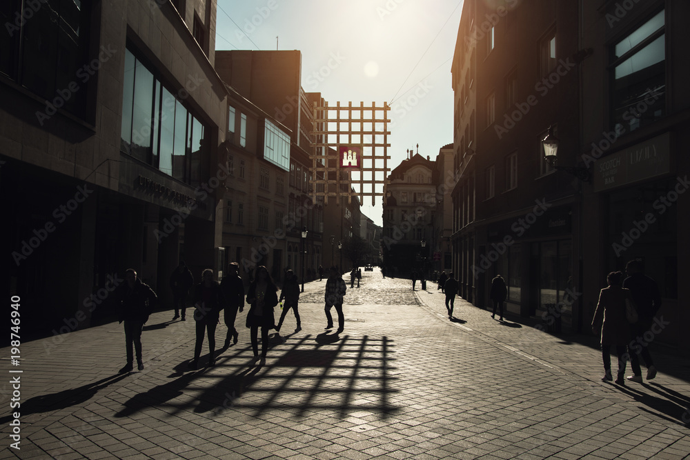 BRATISLAVA SLOVAKIA - APRIL 1, 2018:  Horizontal color image of a silhouetted tourists/people walking on a sidewalk located in Old town city center while the sun is beautifully shining on the ground.