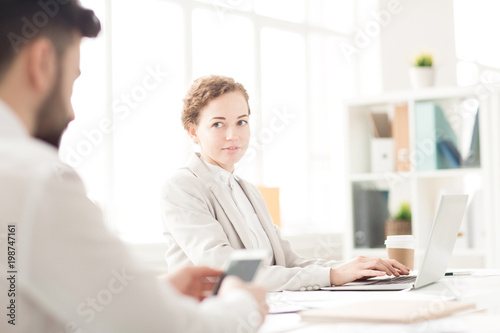 Young businesswoman typing on laptop with her colleague using phone at the table