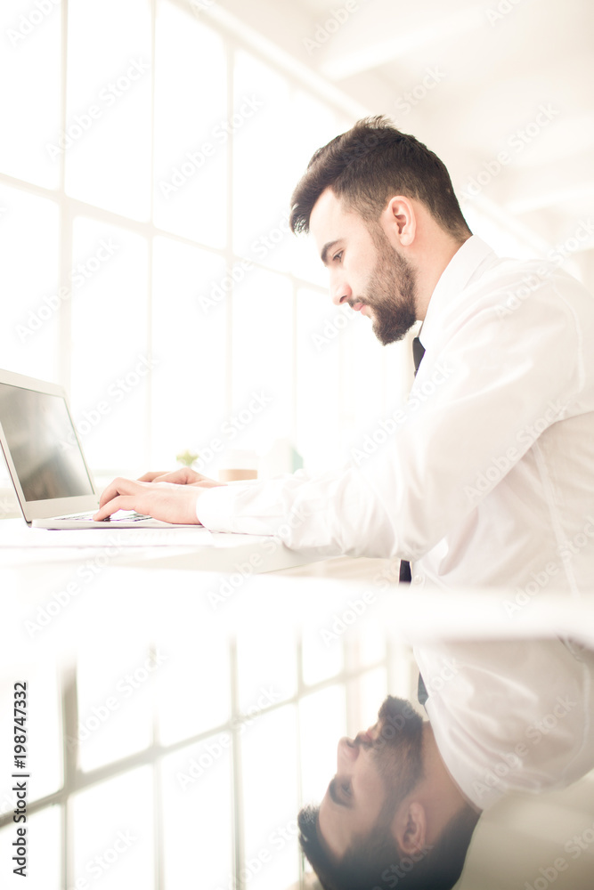 Serious young businessman working on laptop at his workplace Serious young businessman working on laptop at his workplace