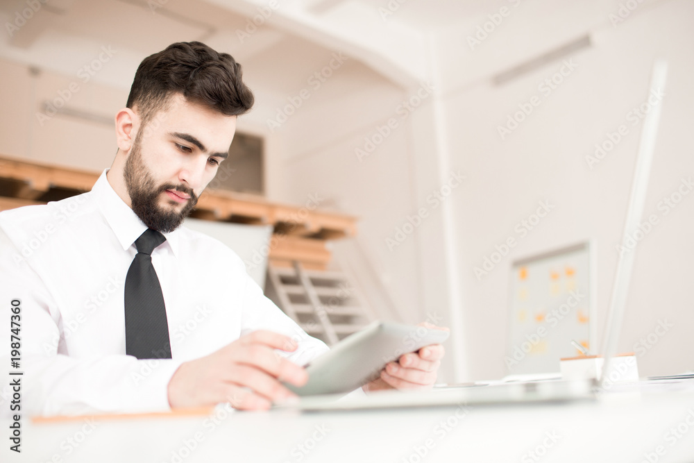 Young businessman sitting at the table and using digital tablet