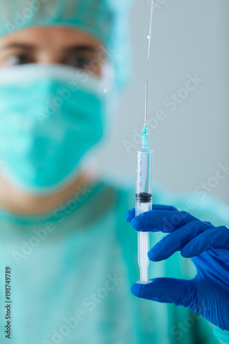 Young woman doctor with blue eyes wearing a cap and face mask showing a syringe