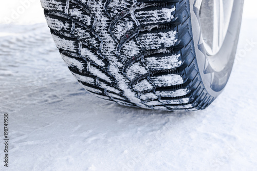 The car tire in the snow close up. Car tracks on the snow. Traces of the car in the snow. Winter tires. Tyres covered with snow at winter road © Aleksei