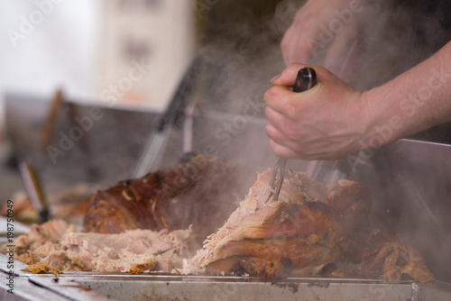 Quadro em tela man carving pork joint with fork and knife at hog roast