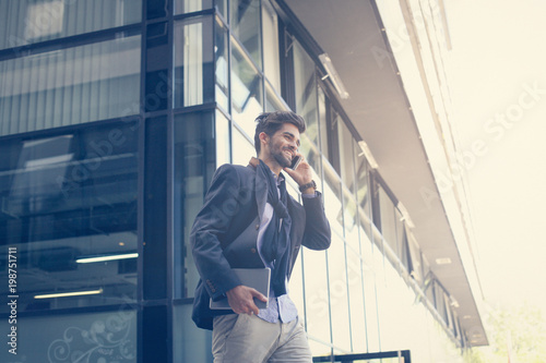 Smiley businessman on street holding iPod and talking on mobile phone. Space for copy.