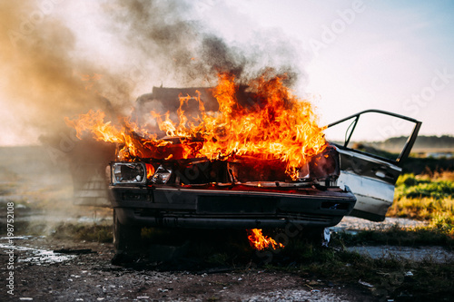 Front of a car burning with a open flames and dark smoke