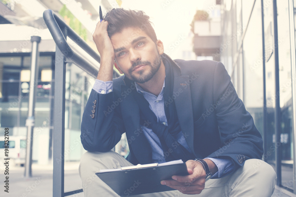 Fototapeta premium Serious businessman sitting on city street and holding document.