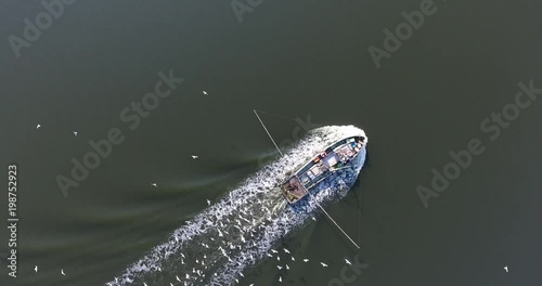 Top view of a small fishing boat with a motor in the middle of the river with a pack of hungry seagulls photo