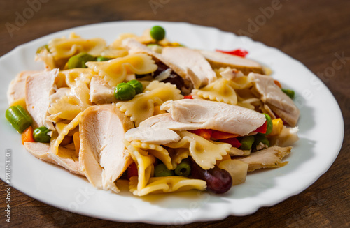 farfalle pasta salad with chicken breast fillet and vegetables in plate on wooden background