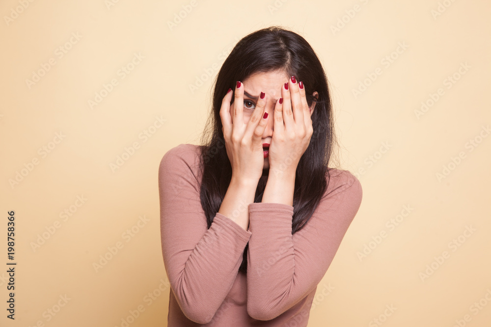 Beautiful young Asian woman peeking through fingers.