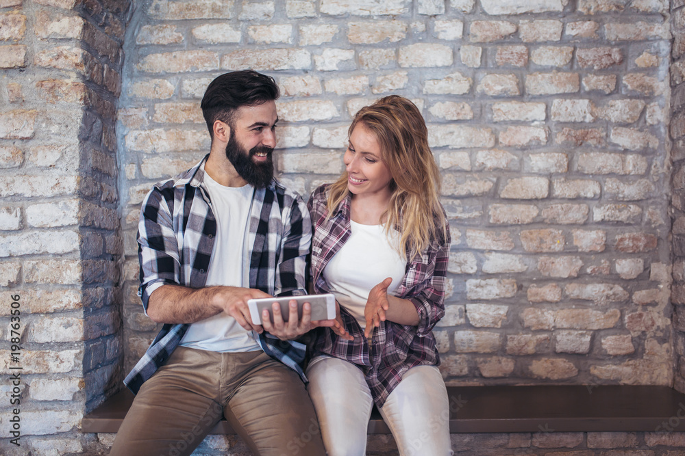 Happy young couple using digital tablet on a brick wall background