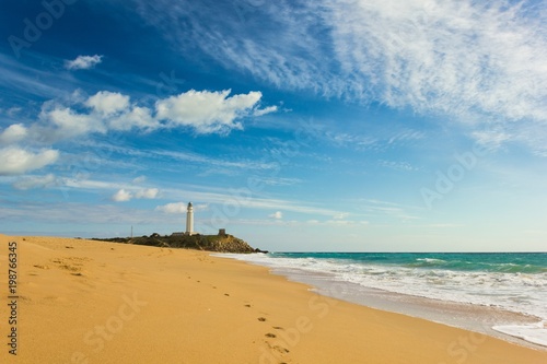 Footsteps on sand by seashore in Zahora beach leading to Trafalgar lighthouse on sunny day in the province of Cadiz, South of Spain photo