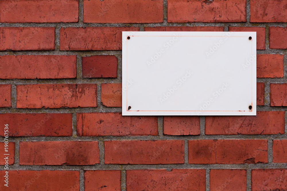Ein weisses unbeschriftetes Schild auf einer roten Ziegelwand Ein weisses unbeschriftetes Schild auf einer roten Ziegelwand