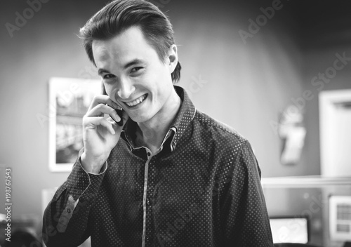 portrait of a young smiling guy in a shirt in an office environment talking on a mobile phone, black and white image