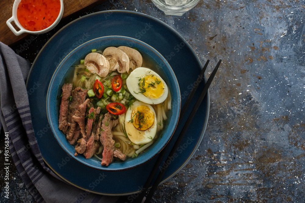 Asian ramen soup with beef, egg, chives, mushrooms in bowl on dark background. Copyspace. Top view Asian ramen soup with beef, egg, chives, mushrooms in bowl on dark background. Copyspace. Top view