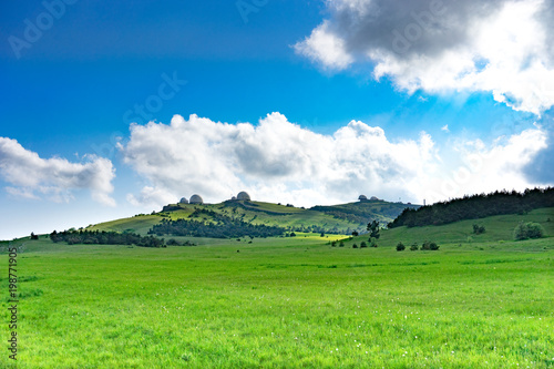 Natural landscape with a green field covered with grass under the blue sky with clouds.