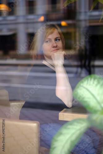 Portrait of attractive redhead plus size woman sitting in cafe, photo throught the glass