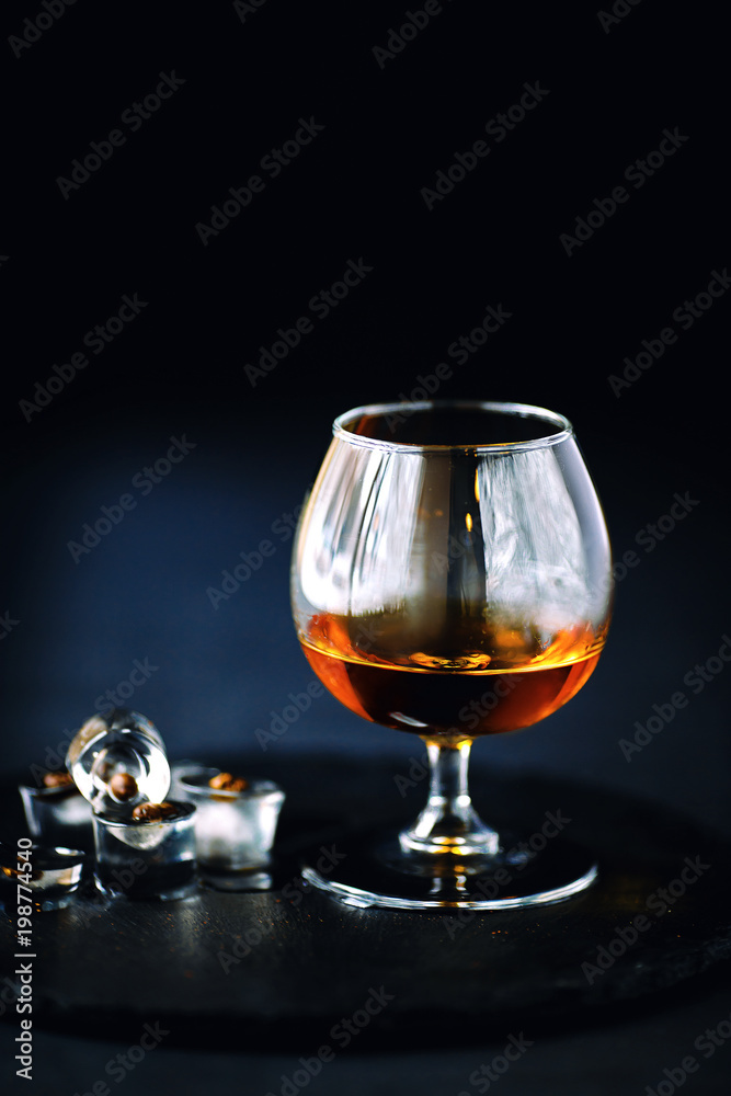 a glass of cognac on a black background, apperetiv with ice and coffee beans a glass of cognac on a black background, apperetiv with ice and coffee beans