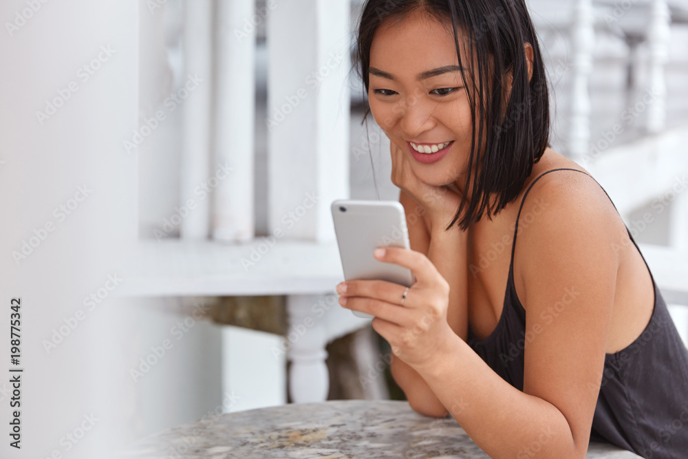 Attractive glad Chinese woman chats in social networks online, uses smart phone for communication, enjoys leisure time. Positive young adorable mixed race female watches video on popular blog Attractive glad Chinese woman chats in social networks online, uses smart phone for communication, enjoys leisure time. Positive young adorable mixed race female watches video on popular blog