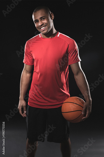 Full length portrait of happy handsome african man in red t-shirt with basketball. Guy joyful looking at camera while feeling easy and relaxed. Isolated