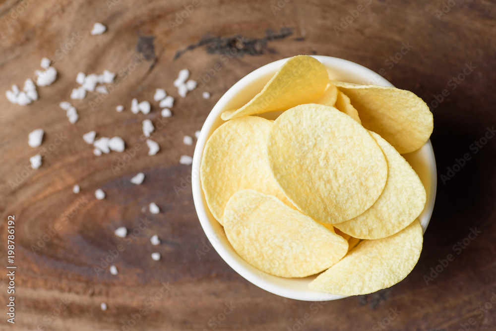 Potato chips in a bowl and salt on wooden background, top view of food Potato chips in a bowl and salt on wooden background, top view of food