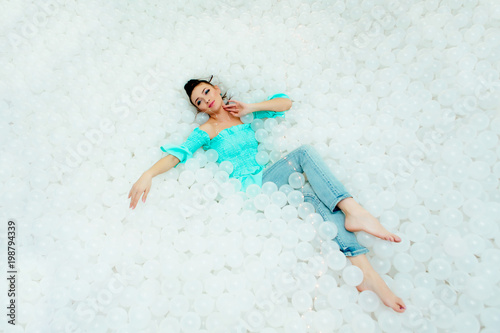 Happy beautiful woman lays surrounded by white plastic balls in the dry pool for adult. Copy space. photo