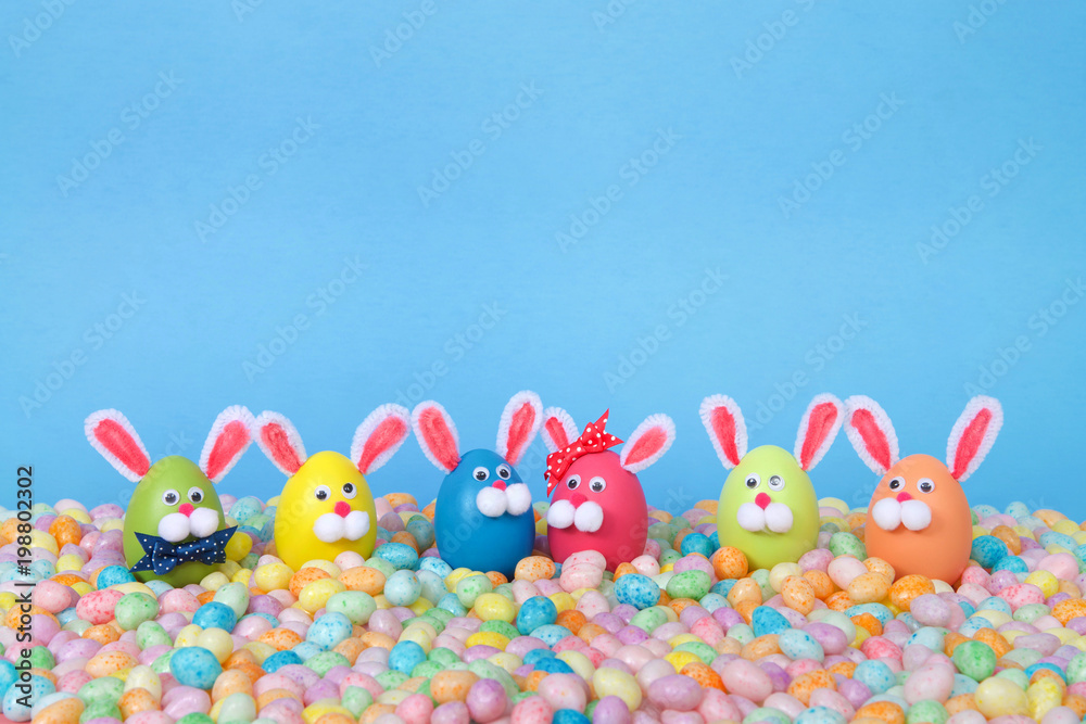 Craft Easter Bunnies made from plastic eggs standing in pastel jelly beans with a light blue background. Fun Easter line up with copy space